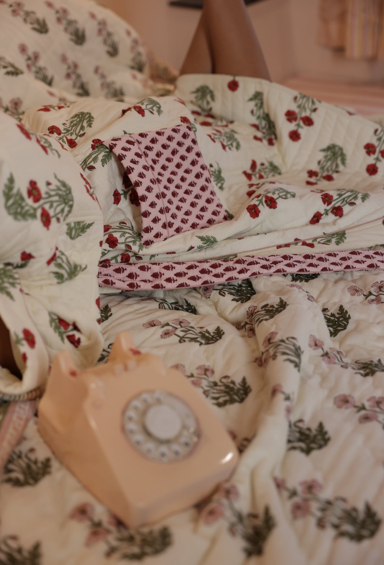 Model laid in condicote poppy dressing gown on a bed with an old fashioned phone