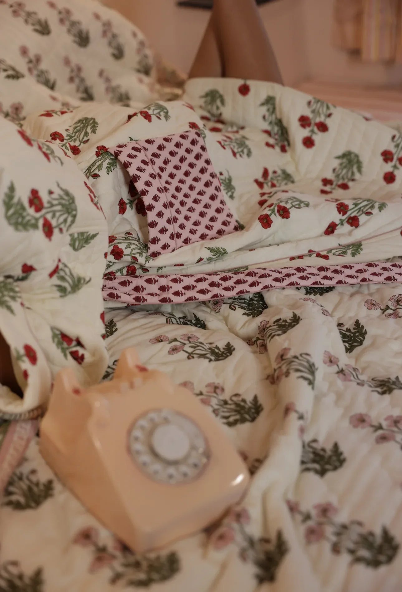 Model laid in condicote poppy dressing gown on a bed with an old fashioned phone