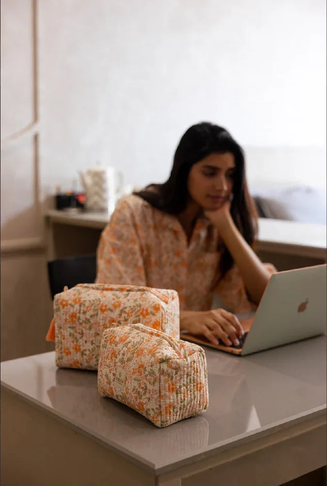 Woman using a laptop with floral wash bags on a table in a kitchen setting.