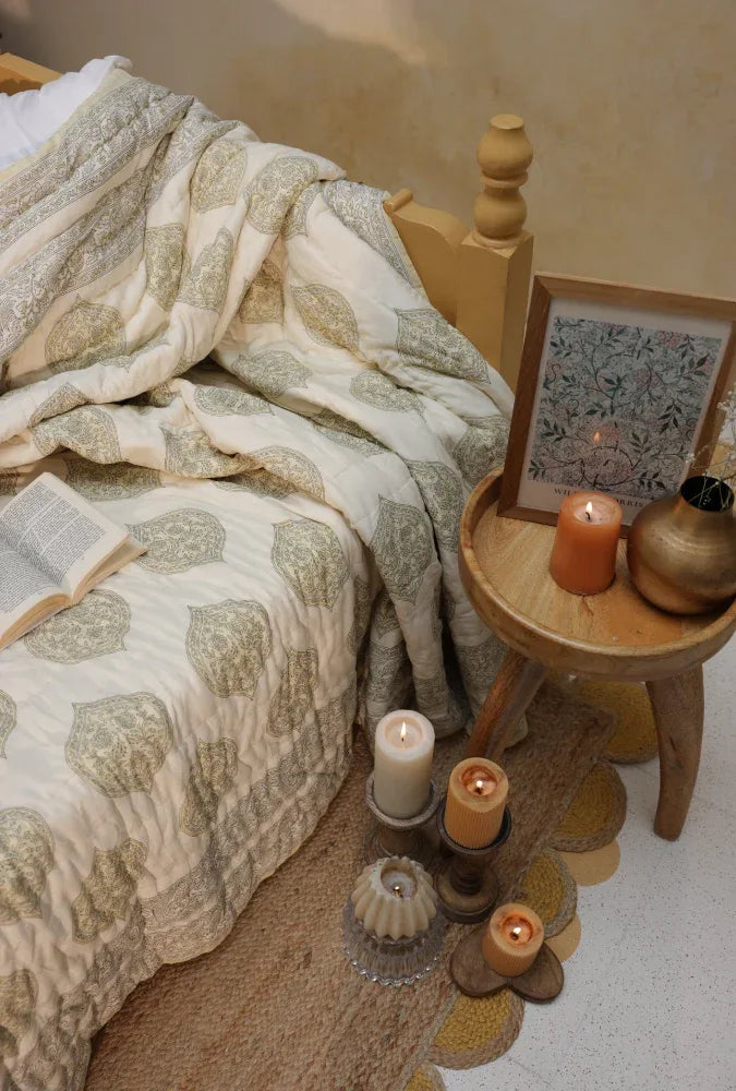 Cosy bedroom scene with a kiftsgate stone bedspread, candles, and decorative items on a wooden side table.