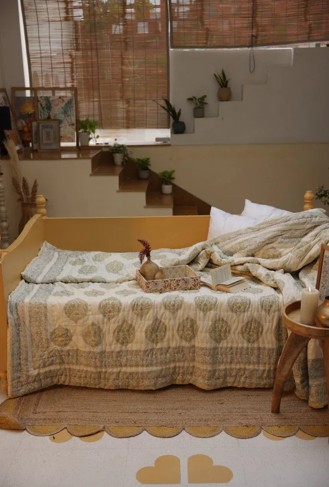 Cosy bedroom with a bed covered in kiftsgate stone quilt and a small table with a candle.