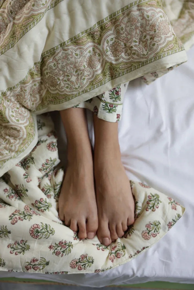 Feet peeking out from under a floral-patterned quilt on a bed.