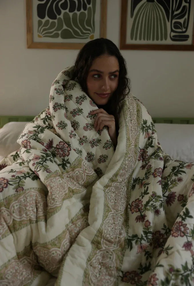 Woman wrapped in a floral quilt in a bedroom.