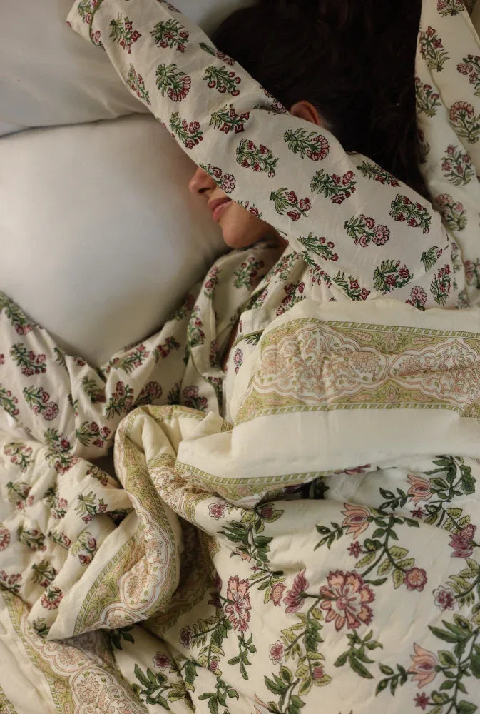 Person lying in bed with floral paxford willow quilt