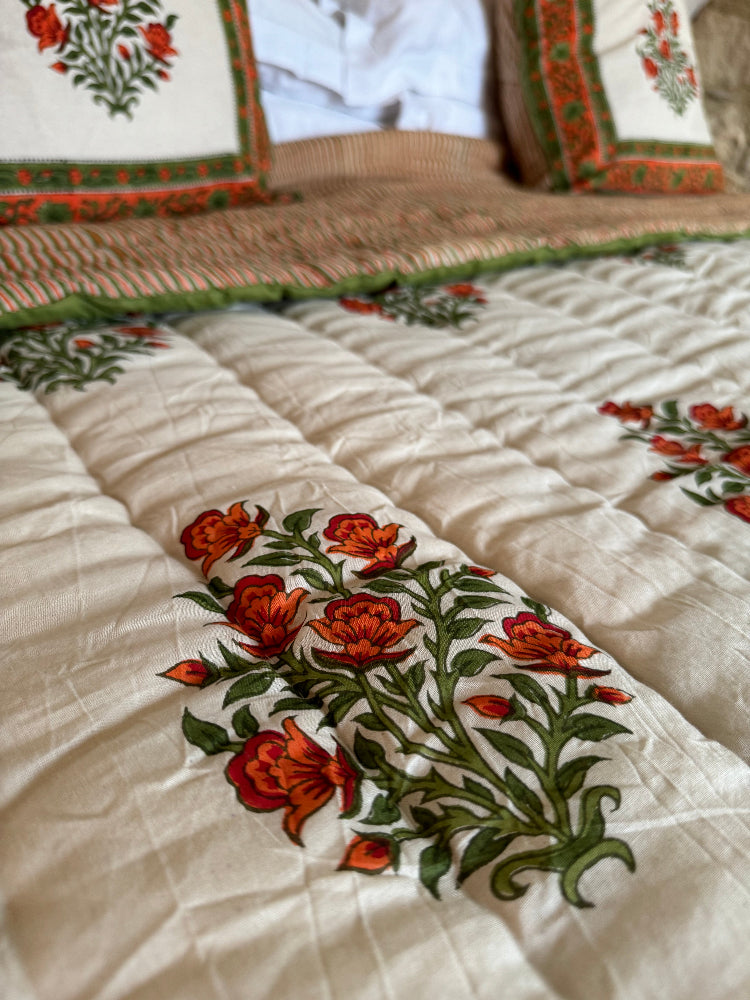 Close-up of a Wilson amber floral quilted bedspread with orange and red flowers and green leaves on a cream background.