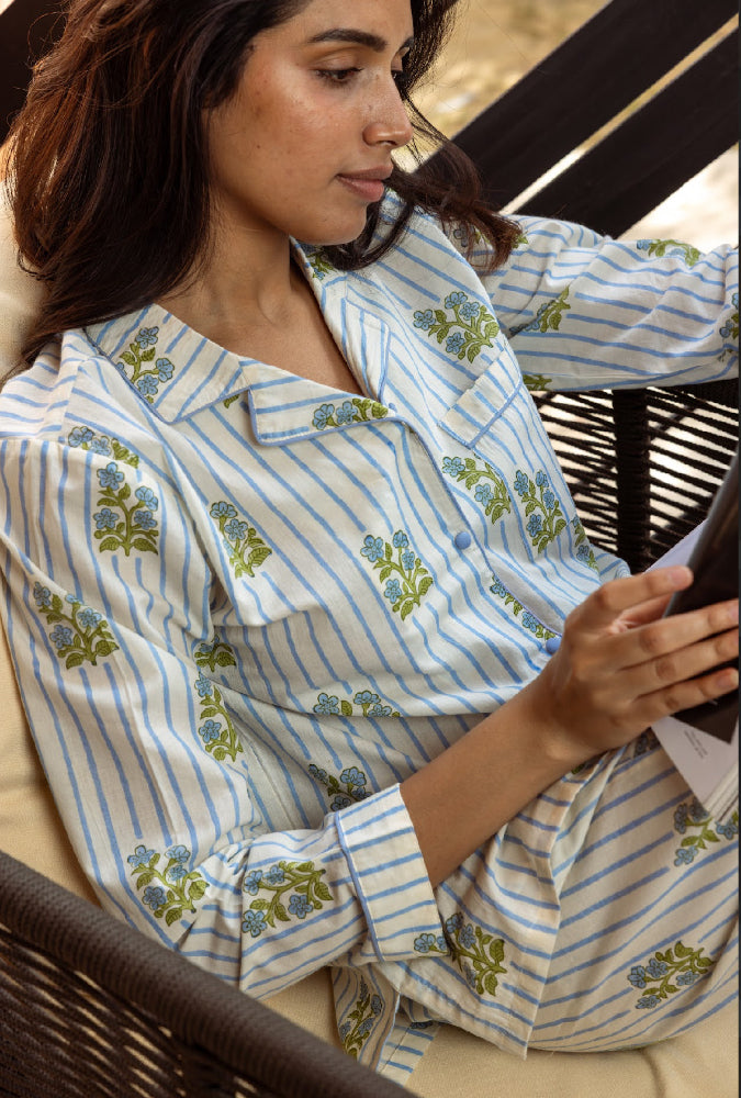 Woman wearing a blue and white striped  pyjamas with floral patterns, sitting on a wicker chair.