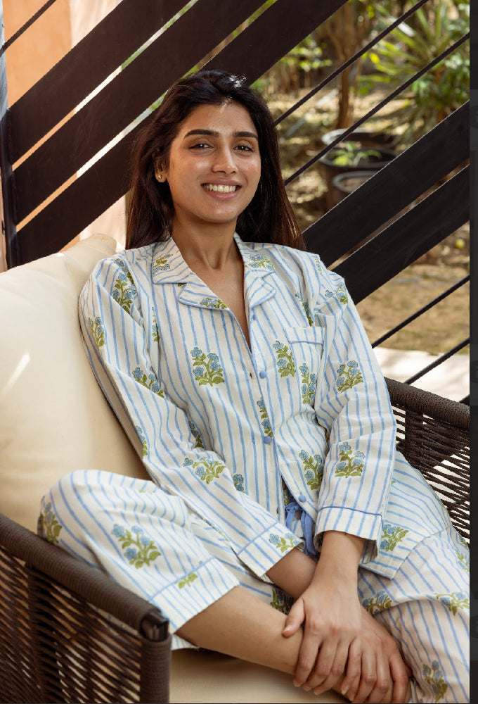 Woman wearing a light blue and white striped pajama set with floral patterns, sitting on a wicker chair.