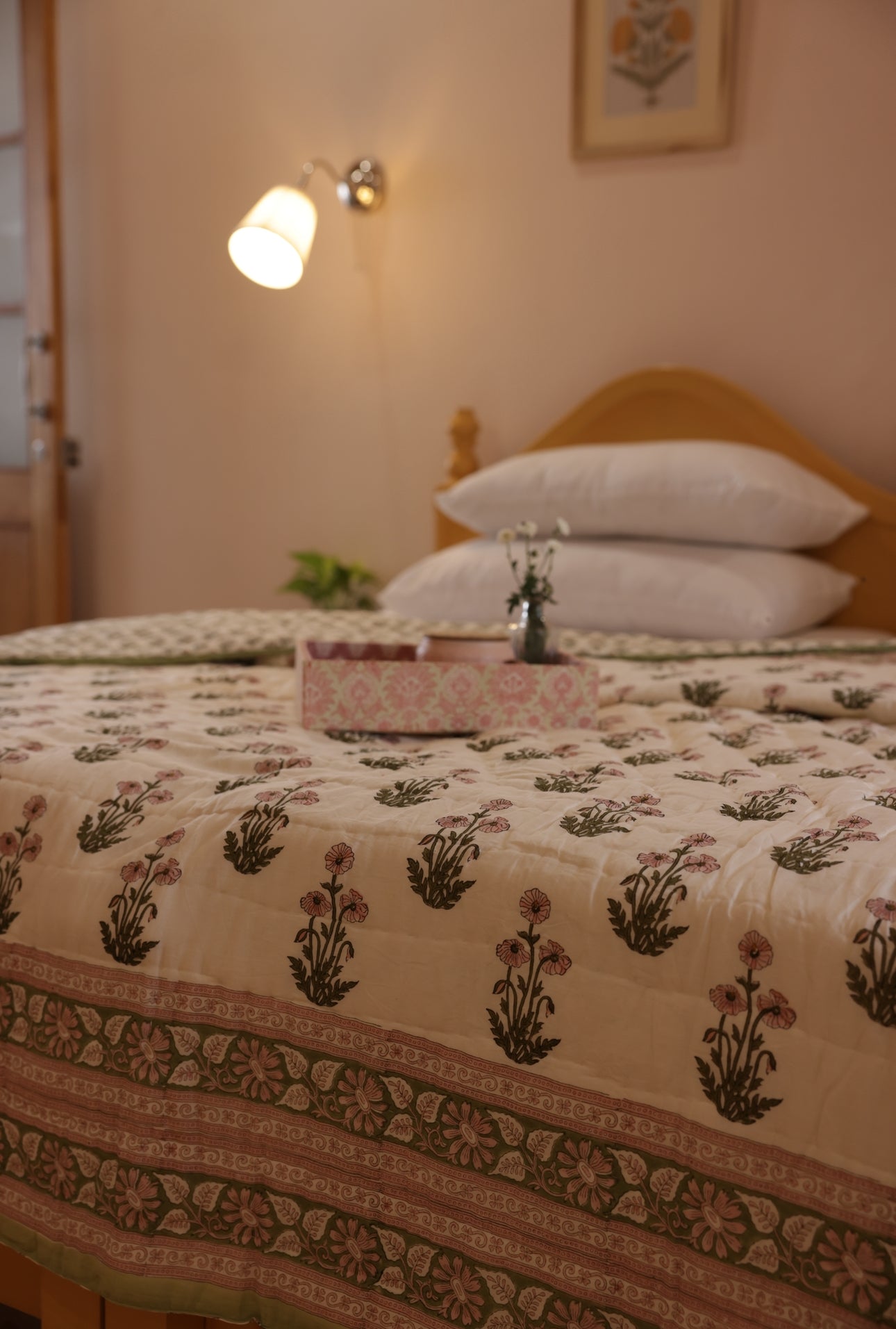 A bed with a condicote poppy quilted bedspread featuring a floral block print design, in a room with tray and wall lighting.