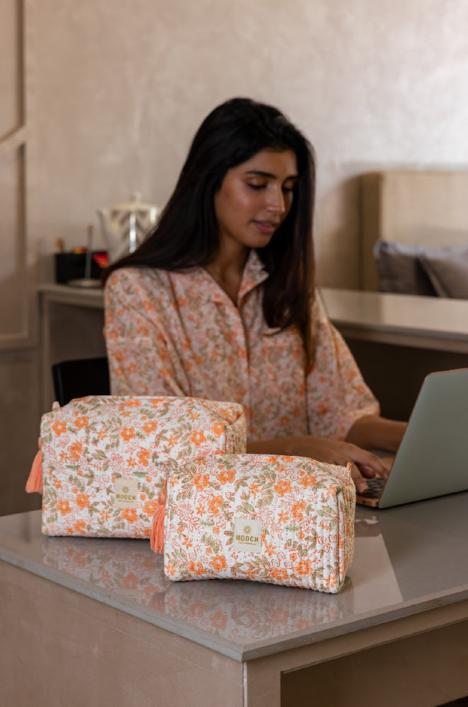 Woman working on a laptop with floral-patterned cosmetic bags on a desk.