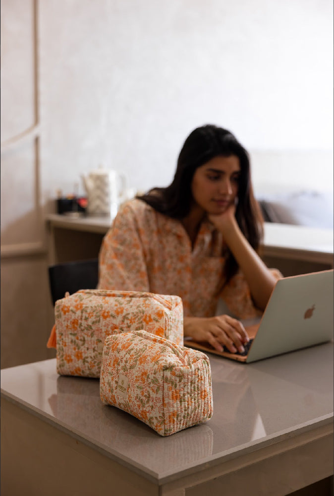 Woman using a laptop with floral wash bags on a table in a kitchen setting.