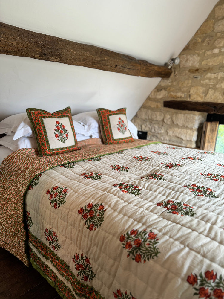 Wilson amber quilt and cushions on a bed in a rustic bedroom with stone walls and wooden beams.